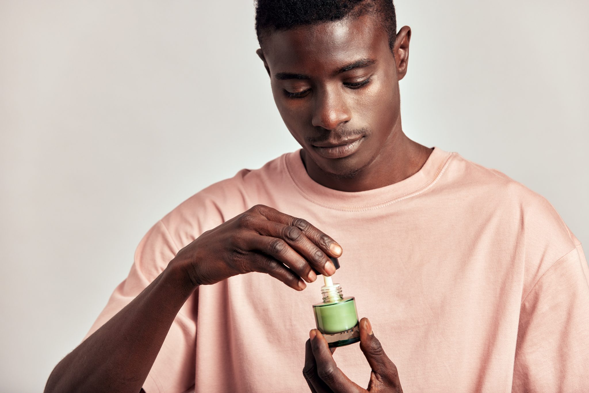 Young black guy holding a vial of facial mask cream in his hands before applying it on his face during his skincare routine. Man caring for the skin to maintain his youthful and healthy appearance